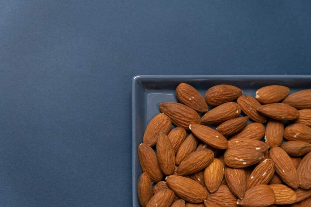Top view of organic almonds in a ceramic dish with a blue background.
