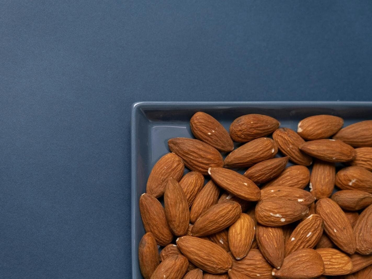 Top view of organic almonds in a ceramic dish with a blue background.