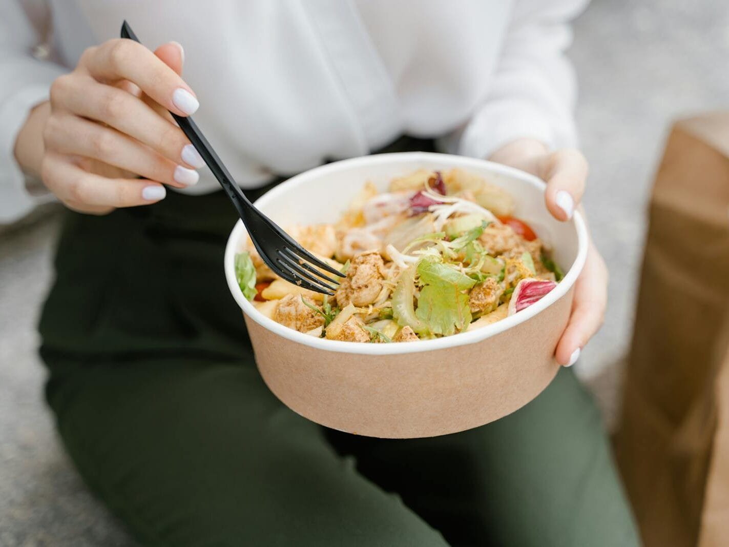 Close-up of a woman eating a fresh salad outdoors, exuding healthy and casual vibes.